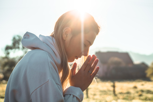 Το πρωί κορίτσι έκλεισε τα μάτια της, προσεύχεται σε εξωτερικούς χώρους, τα χέρια διπλωμένα στην έννοια της προσευχής για την πίστη, την πνευματικότητα, την έννοια της θρησκείας. - Φωτογραφία, εικόνα