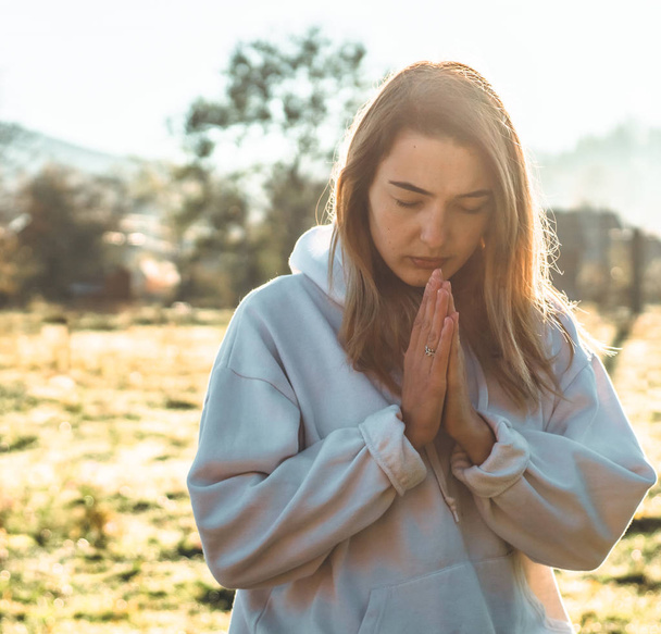 祈り信仰、精神世界、宗教概念の概念で折り返されている女の子は彼女の目を閉じ、屋外に祈って朝、手. - 写真・画像