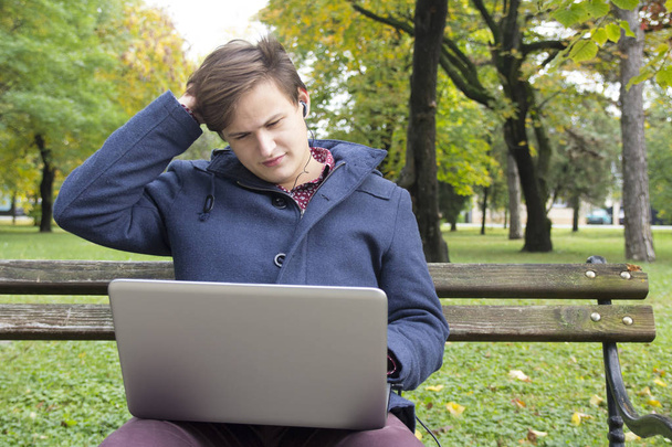 Jeune homme avec ordinateur portable dans le parc, foyer sélectif et petite profondeur de champ, fusée éclairante
 - Photo, image