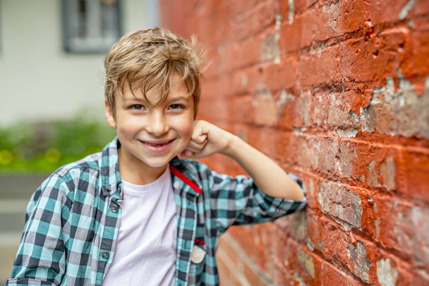 Adorable cute boy staing near a red brick wall - Fotó, kép