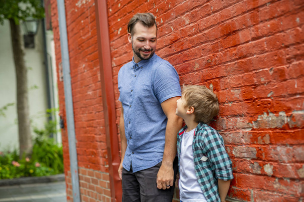 Staing αξιολάτρευτο χαριτωμένο αγόρι κοντά σε ένα τοίχο κόκκινο τούβλο με τον πατέρα του - Φωτογραφία, εικόνα