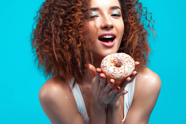 Beautiful young cheerful girl with donut in hand. Fun, food and holiday concept - Foto, Bild