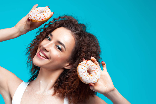 Beautiful young cheerful girl with donuts in hand. Fun, food and holiday concept - Foto, afbeelding