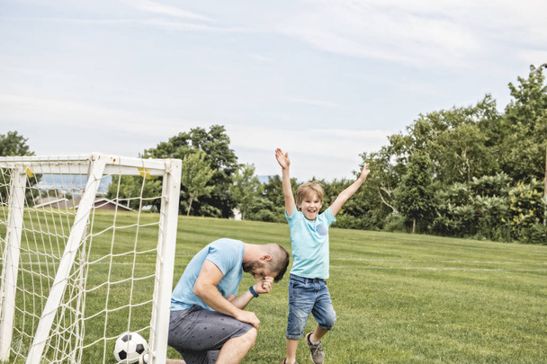 Man with child playing football outside on field - Valokuva, kuva