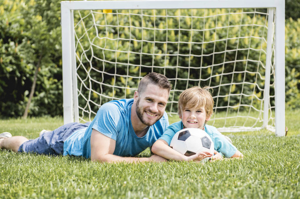 Mann mit Kind spielt draußen auf Feld Fußball - Foto, Bild