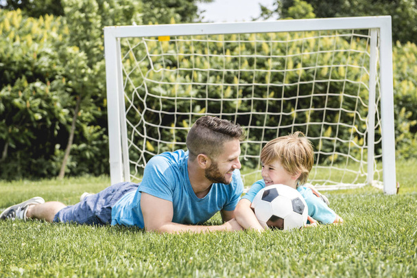 Man with child playing football outside on field - Φωτογραφία, εικόνα