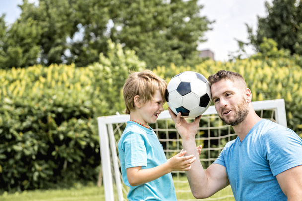 Man with child playing football outside on field - Foto, Bild