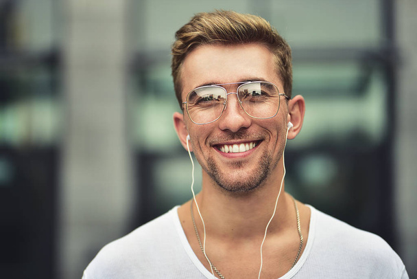 Ihmiset, teknologia, matkailu ja matkailu - mies, jolla on kuulokkeet, älypuhelin kaupungin kadulla ja musiikin kuunteleminen harmaalla seinällä
 - Valokuva, kuva