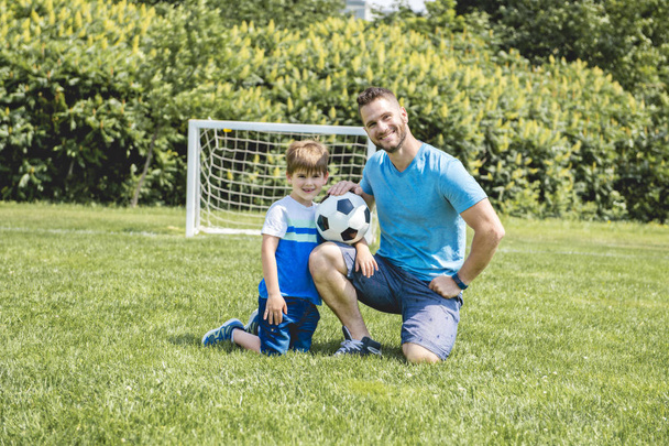 Man with child playing football outside on field - Foto, Imagem