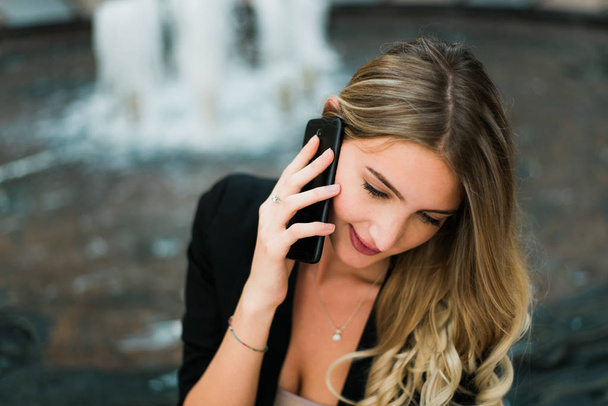 Krásná blondýna úspěšné obchodní žena sedí, mluvil telefonu a s úsměvem. - Fotografie, Obrázek