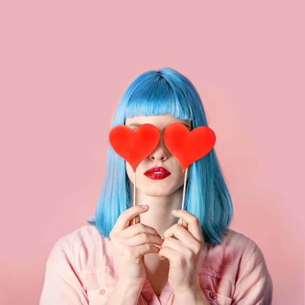 Young stylish woman with blue hairstyle and red lipstick holding valnetine's heart on her eyes. Hipster funny girl model over pink pastel studio background. Love and valentine's day design concept. - Photo, Image
