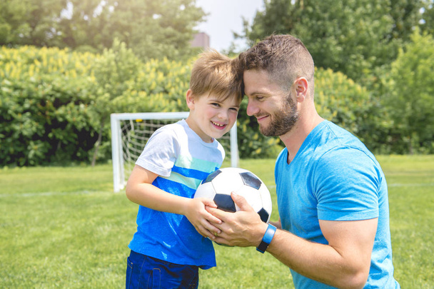 Man with child playing football outside on field - Foto, imagen