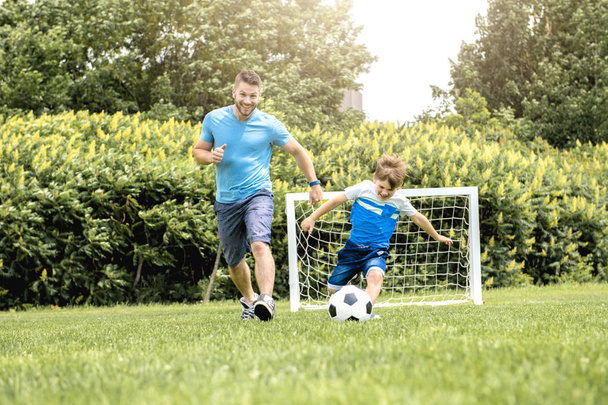 Man with child playing football outside on field - Foto, immagini