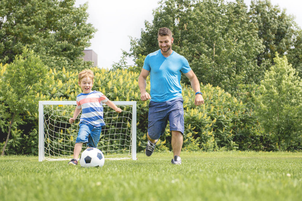 Man with child playing football outside on field - Photo, Image