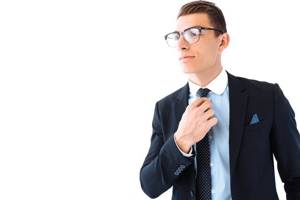 Successful businessman in glasses and suit, carefully straightens tie and posing on isolated white background - 写真・画像