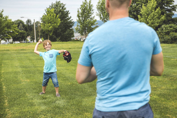 Handsome dad with his little cute sun are playing baseball on green grassy lawn - Foto, Imagen
