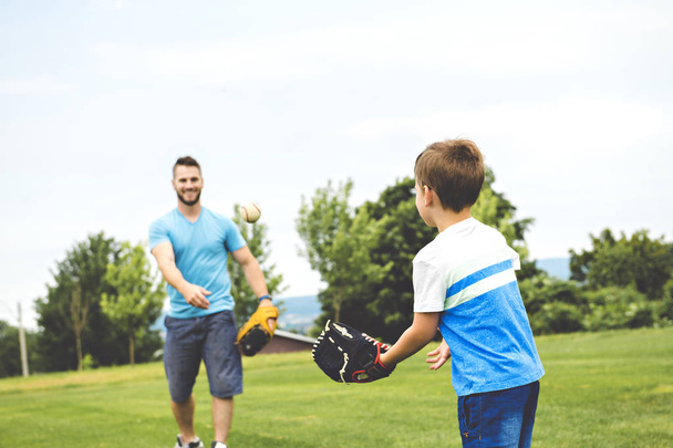 Handsome dad with his little cute sun are playing baseball on green grassy lawn - Foto, immagini