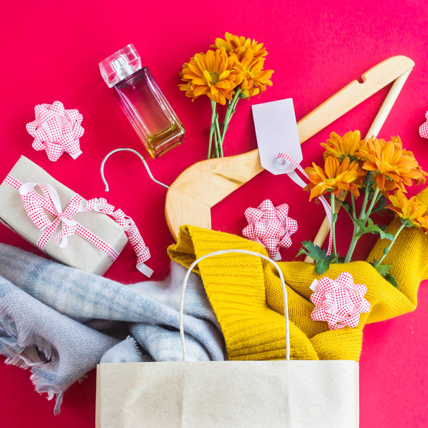 Papierbastelpaket mit Einkäufen für Frauen - Kleidung, Geschenke, Parfüms, Blumen und Kleiderbügel. auf leuchtend rotem Hintergrund. Black-Friday-Konzept. Draufsicht, flache Lage - Foto, Bild
