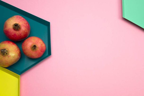 Granatäpfel auf rosa, gelben und grünen Hintergrund. Kreative Herbstgestaltung. Grenzregelung. flache Lageoberseite. Kopierraum. - Foto, Bild