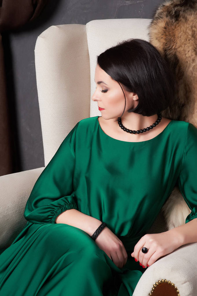 Krásná brunetka žena v hedvábné zelené šaty představují vintage židli. Bohémský styl. - Fotografie, Obrázek