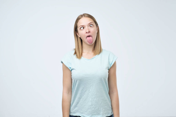 Καυκάσιος γυναίκα δείχνει γλώσσα σε γκρι φόντο. Κάνοντας μορφασμούς έχοντας καλή διάθεση - Φωτογραφία, εικόνα