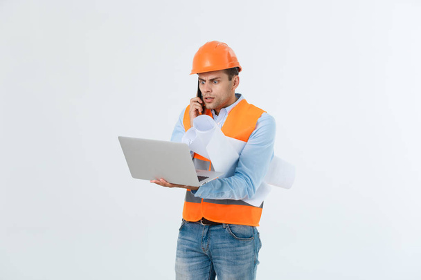 enttäuschter gutaussehender Ingenieur in orangefarbener Weste und Jeans mit Helm, isoliert auf weißem Hintergrund - Foto, Bild