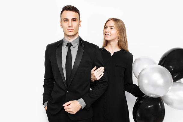 beautiful stylish couple, a young girl in a black dress and a man in a black suit, in the hands, balloons and bags, for shopping on a white background. Concept of shopping, discounts, black friday - Φωτογραφία, εικόνα