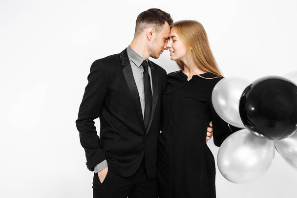 beautiful stylish couple, a young girl in a black dress and a man in a black suit, in the hands, balloons and bags, for shopping on a white background. Concept of shopping, discounts, black friday - Fotoğraf, Görsel