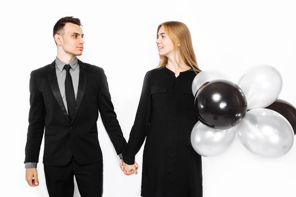 beautiful stylish couple, a young girl in a black dress and a man in a black suit, in the hands, balloons and bags, for shopping on a white background. Concept of shopping, discounts, black friday - Photo, image