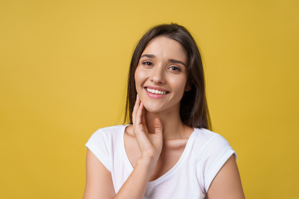 Happy cheerful young woman with joyful and charming smile isolated over yellow background. - 写真・画像
