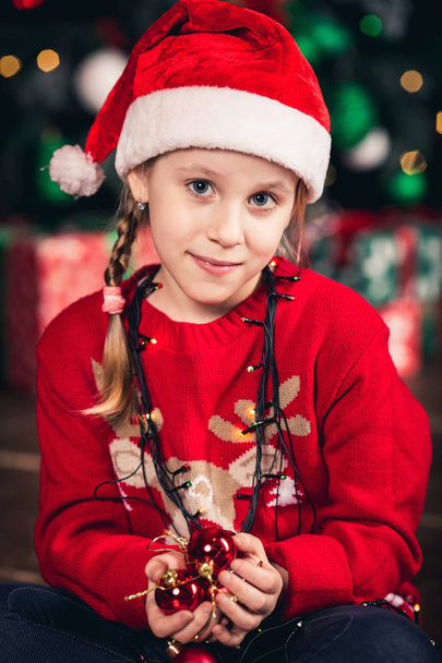 Santa girl zabalené v garland drží vánoční stromeček hračky. - Fotografie, Obrázek