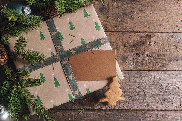 Kerst gifting kader met een geschenk verpakt in bruin papier met kleine sparren met een ongeschreven tag en een Xmas cookie, op een rustieke tafel. - Foto, afbeelding