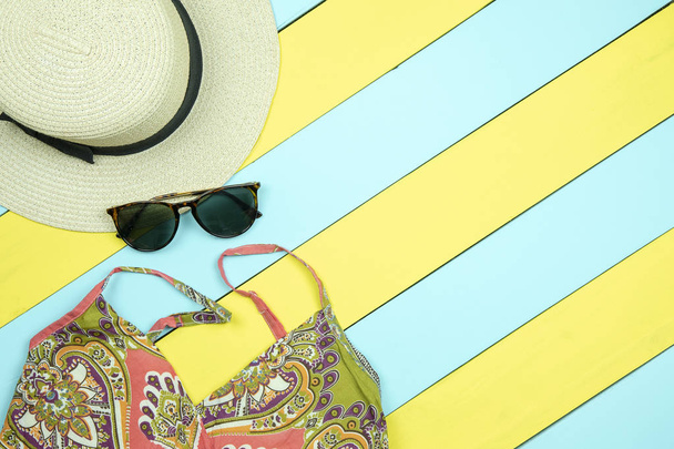 Słomkowy kapelusz, okulary słoneczne, Letnie sukienki na kolor żółty i zielony drewniane tła.  - Zdjęcie, obraz