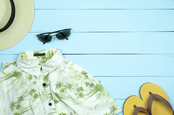 Straw hat, sun glasses, shirt, flip flops on light green wooden background.  - Photo, Image