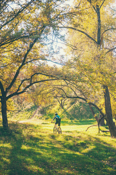 La chica con una mochila monta en bicicleta en el parque de otoño. Mujer delgada entrena en la naturaleza. Deportes en el bosque. Paseos turísticos por un sendero de tierra. Viajar en bicicleta
. - Foto, Imagen