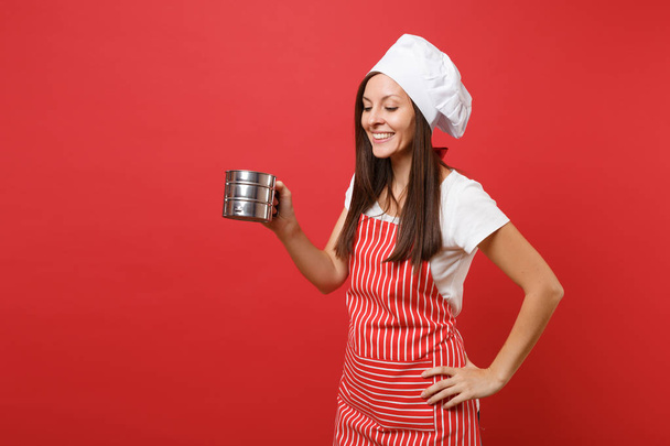 Housewife female chef cook or baker in striped apron, white t-shirt, toque chefs hat isolated on red wall background. Housekeeper woman hold metal iron sieve sifting flour. Mock up copy space concept - Foto, Imagem