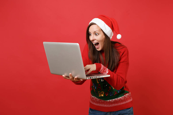 Excited Santa girl keeping mouth wide open looking surprised working typing on laptop pc computer isolated on red background. Happy New Year 2019 celebration holiday party concept. Mock up copy space - Valokuva, kuva
