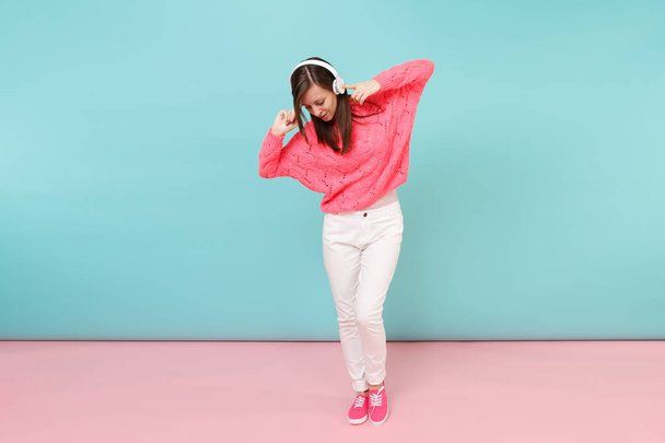 Портрет щасливої молодої жінки в трикотажному рожевому светрі, білих штанях, навушниках ізольовані на яскраво-рожевому синьому пастельному фоні стіни в студії. Концепція модного способу життя. Збільшити простір для копіювання
 - Фото, зображення
