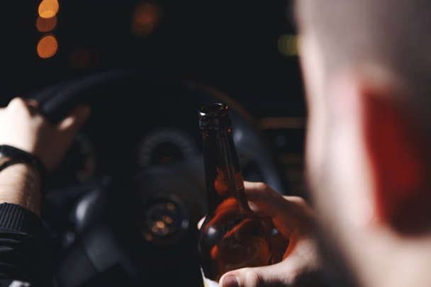Μεθυσμένος νεαρός άνδρας οδηγεί ένα αυτοκίνητο με ένα μπουκάλι μπύρας. Αυτή είναι μια εικόνα της εκστρατείας του «μην πιείτε για αυτοκίνητο." - Φωτογραφία, εικόνα