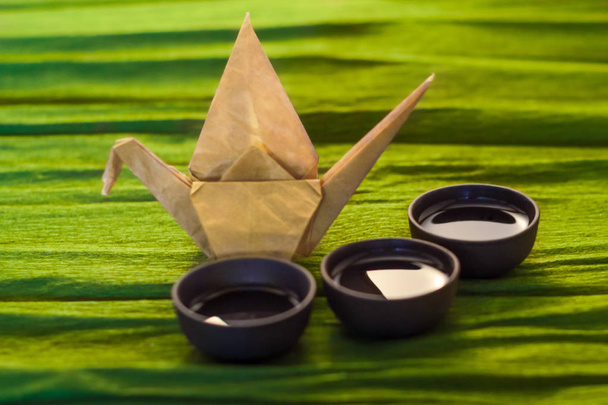 Three cups of ceramics and a origame  crane on the green background, close view - Photo, Image