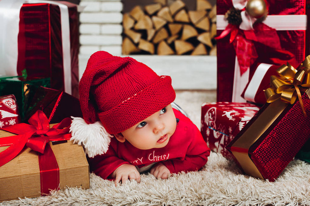 Malý chlapec Santa leží na podlaze v zařízené studio s vánoční dárky. - Fotografie, Obrázek