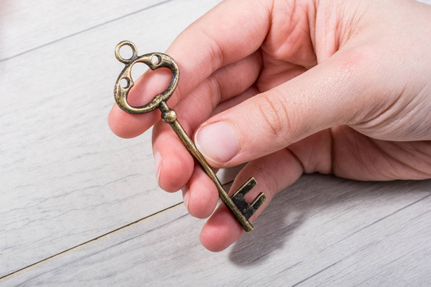 Hand holding a retro styled decorative key on wooden texture - Φωτογραφία, εικόνα