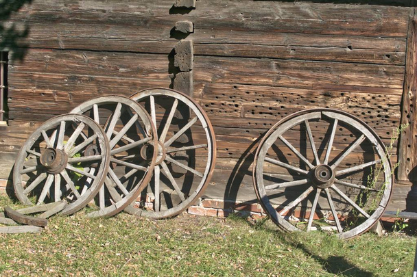 alte Holzräder für Wagen mit Metallringen in der Nähe einer Holzhütte - Foto, Bild
