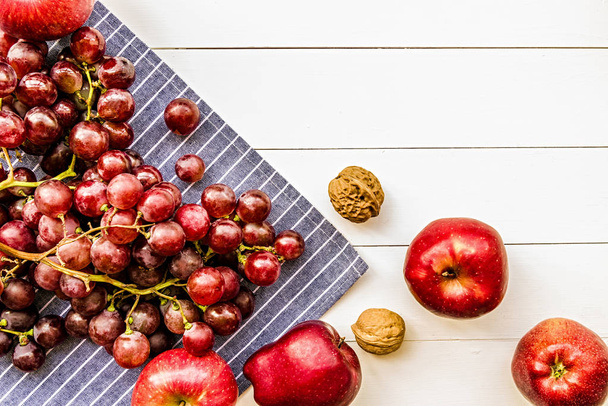 raw purple and red fruit: grapes, apples, walnuts top view on white wooden background flat lay. Healthy food or diet concept - Foto, Bild