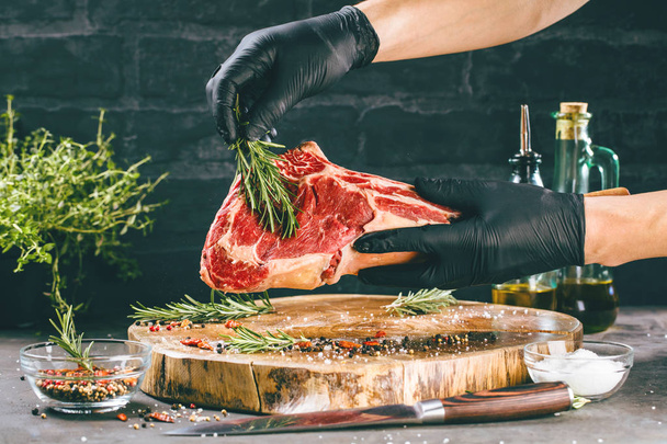 Male hands of butcher or cook holding tomahawk beef steak on dark rustic kitchen table background - Foto, Imagem
