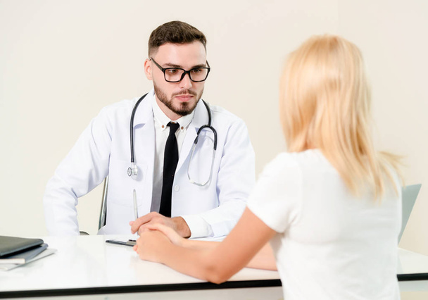 Male doctor is talking to female patient in hospital office. Healthcare and medical service. - Photo, image