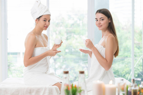 Two women drinking tea or herbal drinks while having conversation in luxury day spa. Wellness, leisure and healthcare concept. - Photo, Image