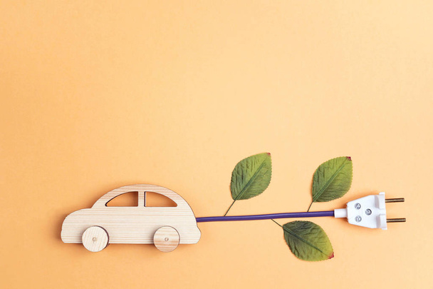 Wooden toy car with electrical cable plug with leaves as an electric car symbol. Save energy concept. Flat lay, copy space, top view. - Фото, зображення