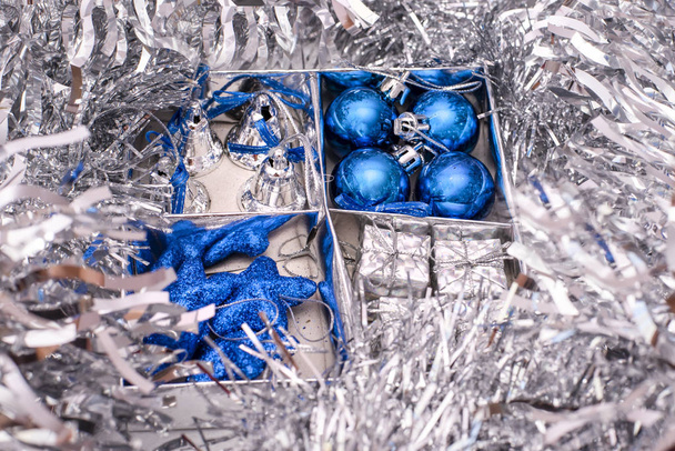 Weihnachtsspielzeug bestehend aus blauen Sternen, blauen Weihnachtskugeln, silbernen Glocken und Geschenkboxen in Schachtel zwischen den silbernen - Foto, Bild
