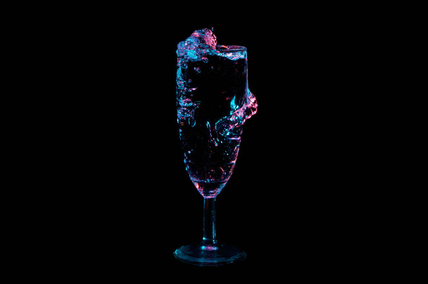 Nestemäinen roiskeita ja halaus lasi alla sininen ja punainen valot eristetty musta tausta
 - Valokuva, kuva